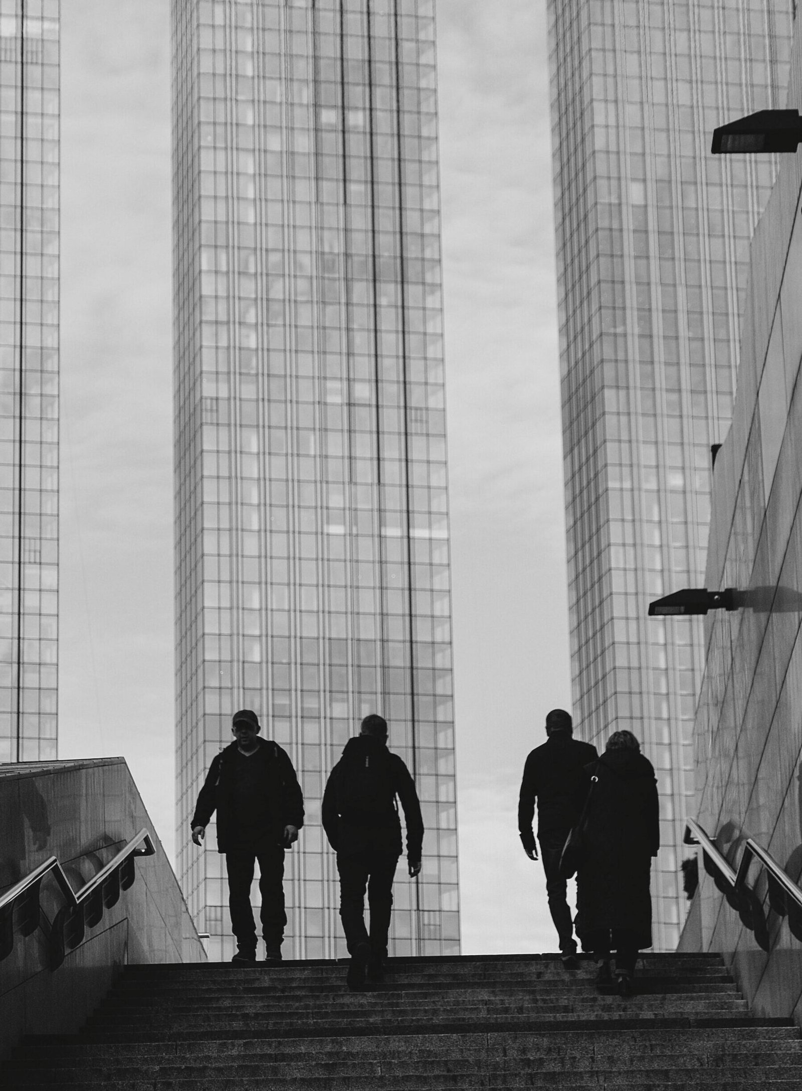 Silhouetted pedestrians in an urban landscape by skyscrapers in black and white.