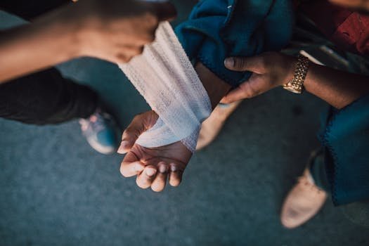 A detail shot showing hands applying a bandage to an injured wrist outdoors. acidente
