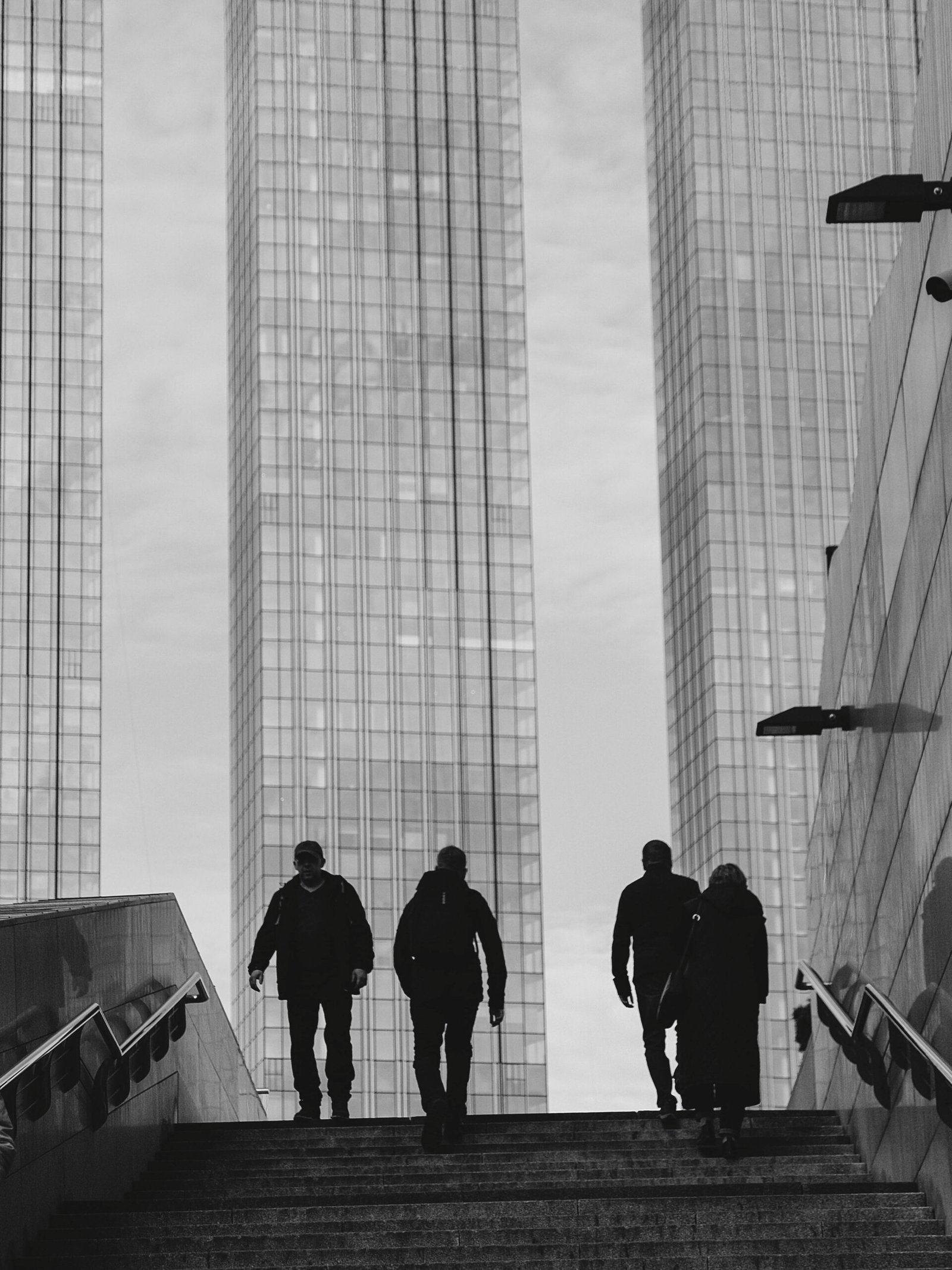 Silhouetted pedestrians in an urban landscape by skyscrapers in black and white.