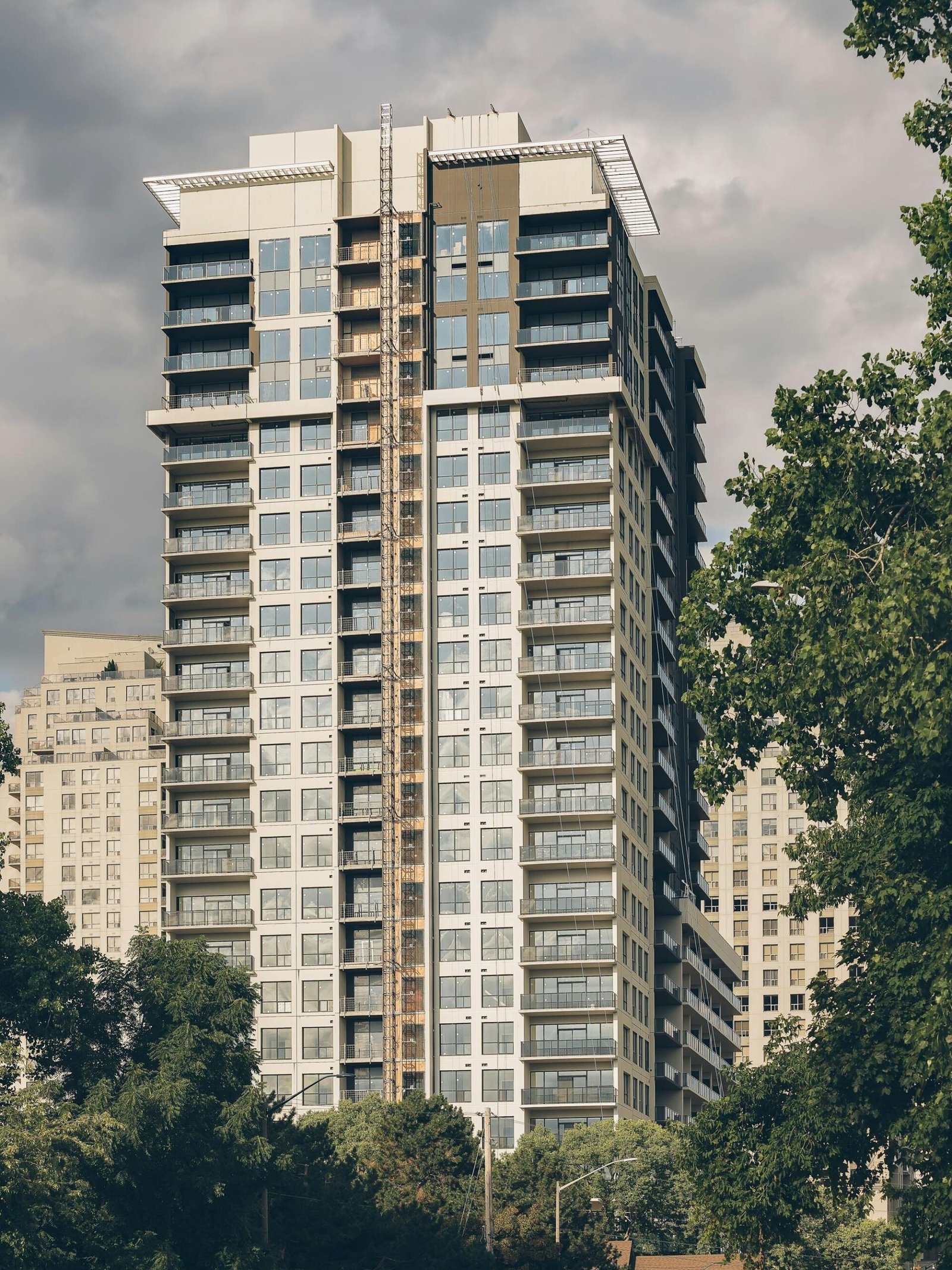 Tall residential skyscraper with modern glass design in urban setting, surrounded by trees.