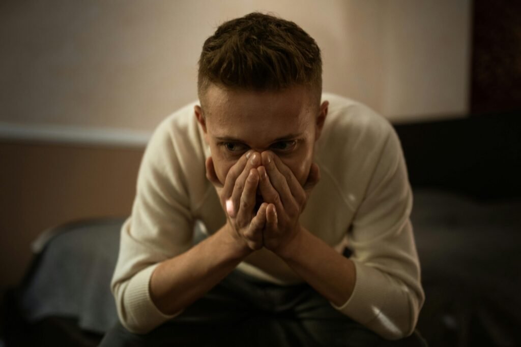 A worried man indoors covering his face with hands, depicting stress or contemplation.