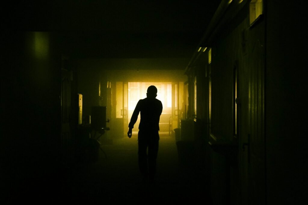 A mysterious silhouette of a person in a dimly lit corridor with dramatic lighting.