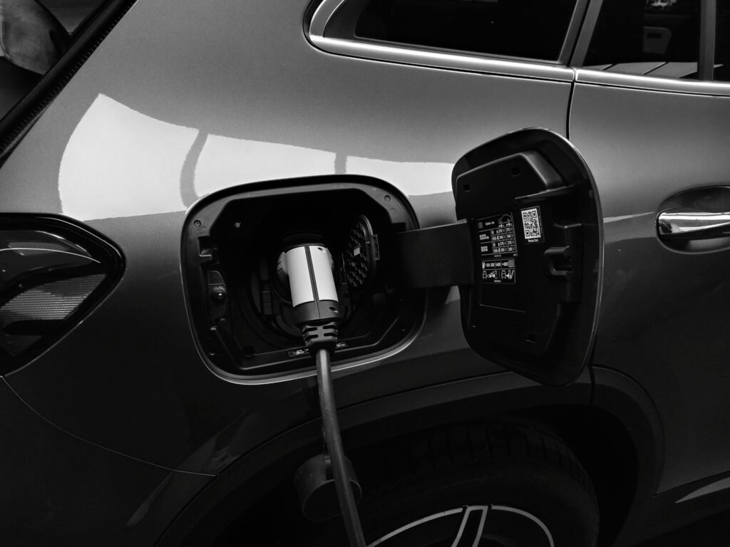 Close-up black and white image of an electric vehicle charging at a station.