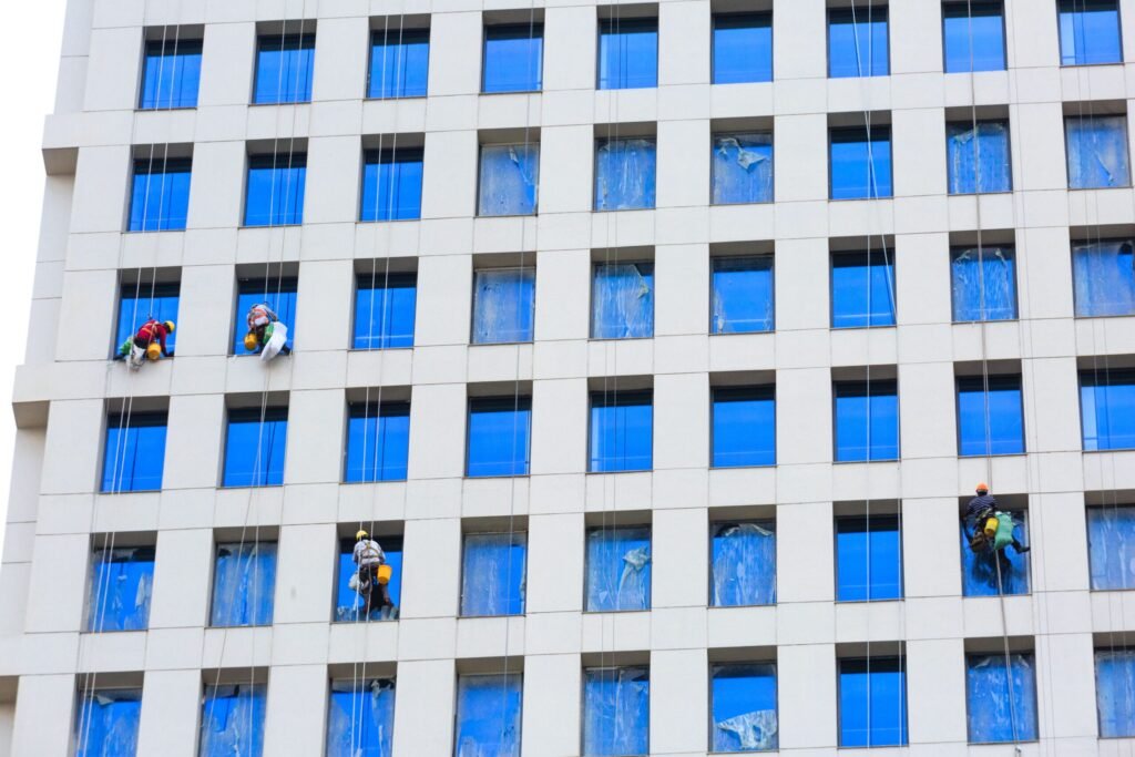 Professional workers clean skyscraper windows using ropes in urban setting.