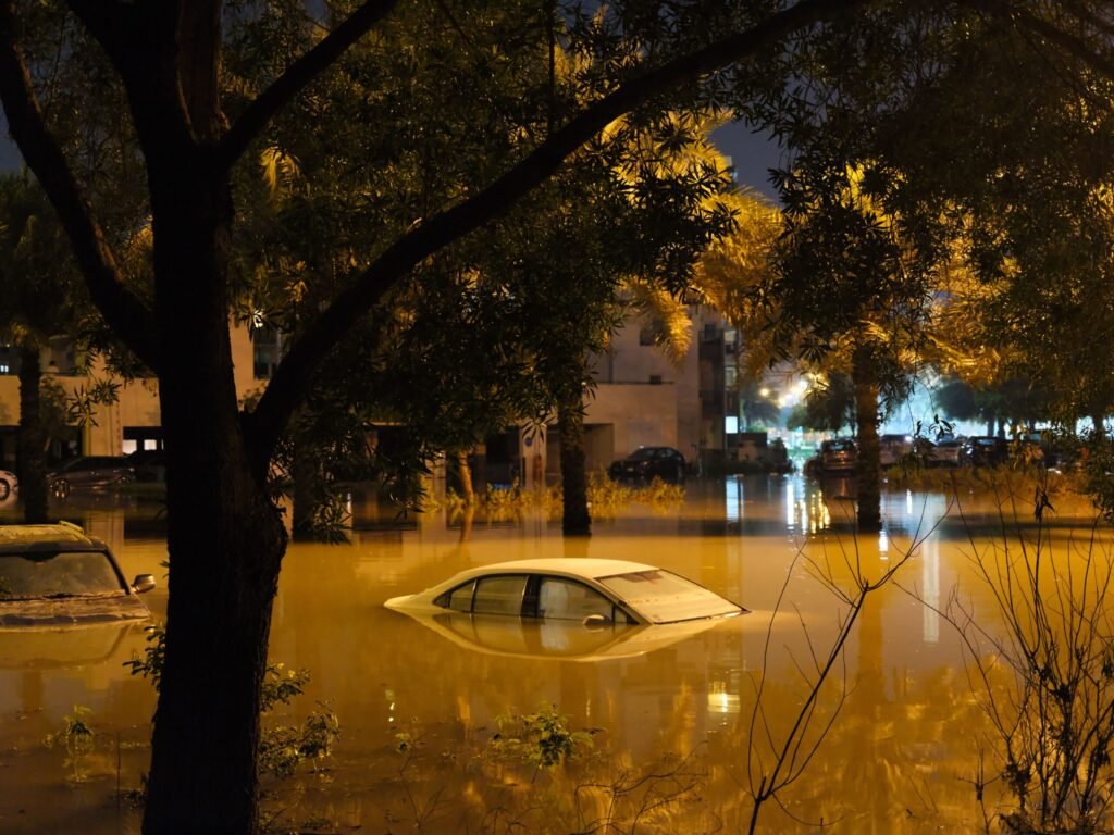 A dramatic scene of submerged cars in a flooded street surrounded by trees at night.