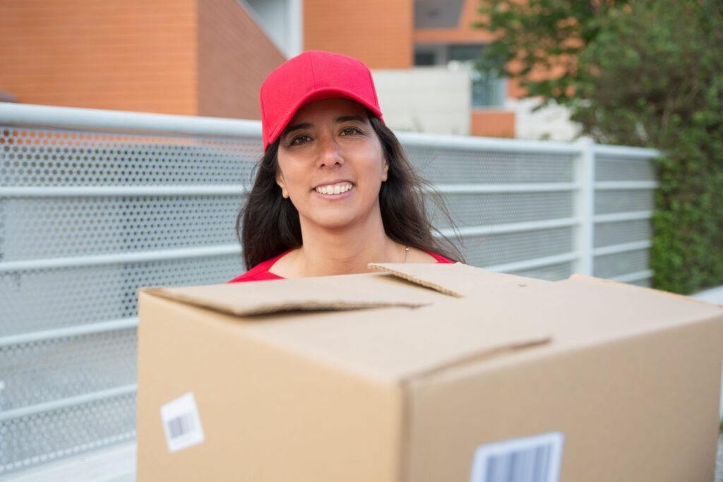 Female courier in red uniform carrying a package outside on a sunny day.